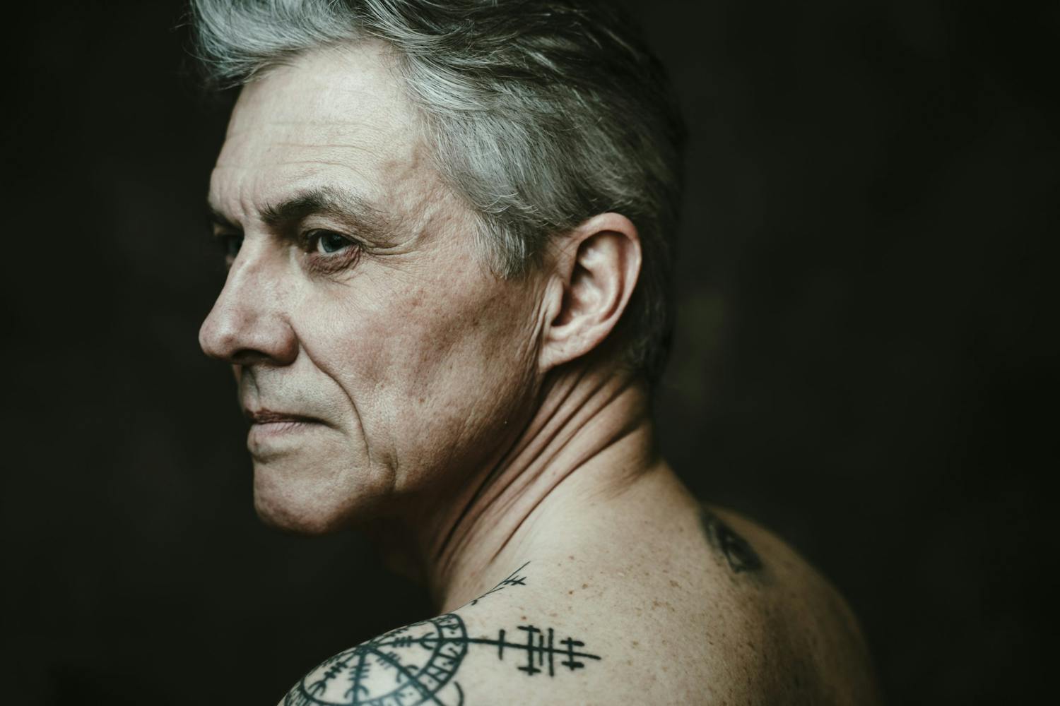 Kahden studiosalaman valaisema mies katsoo ulos kuvan vasemmalla puolella